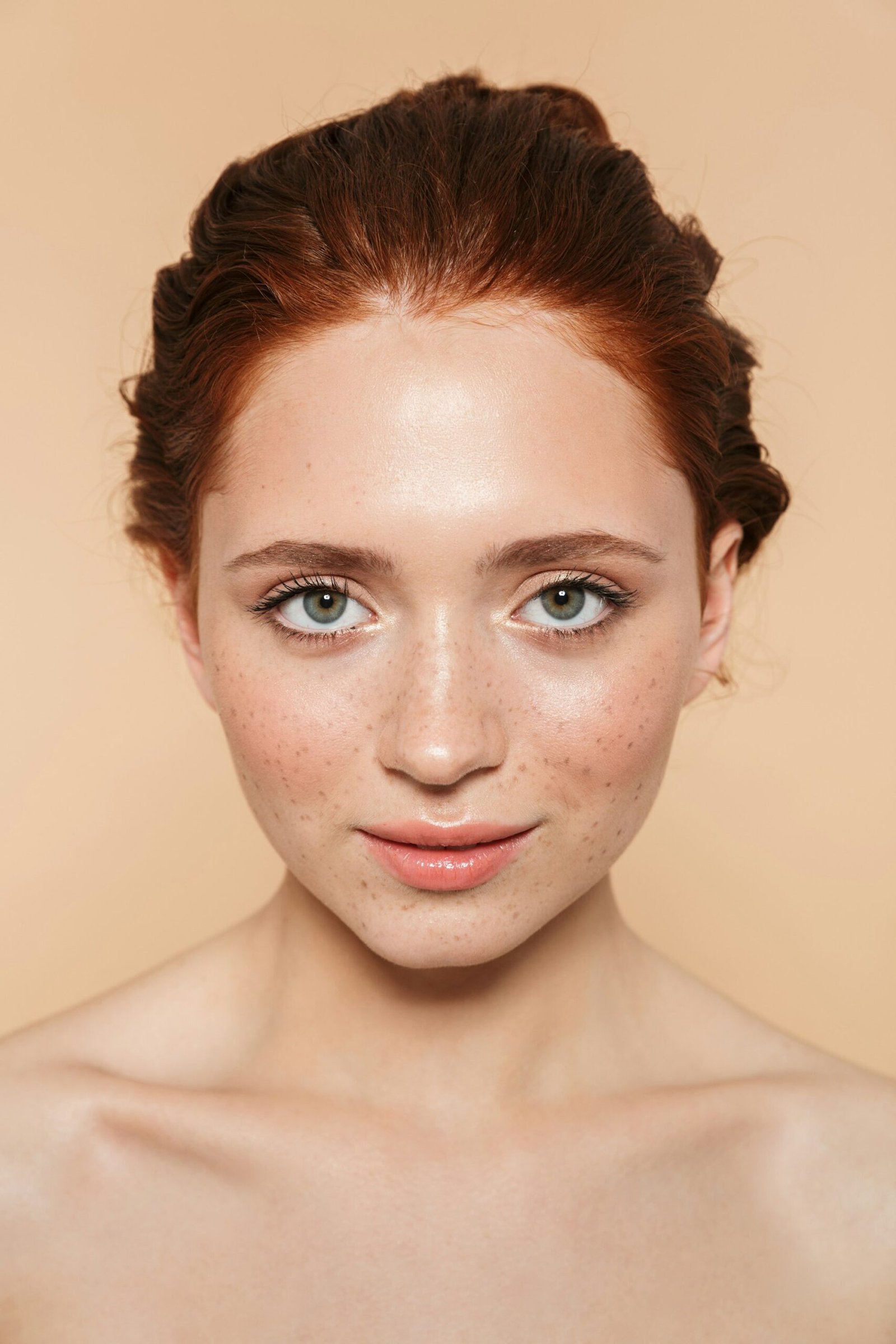 A woman with auburn hair and freckles against a beige background