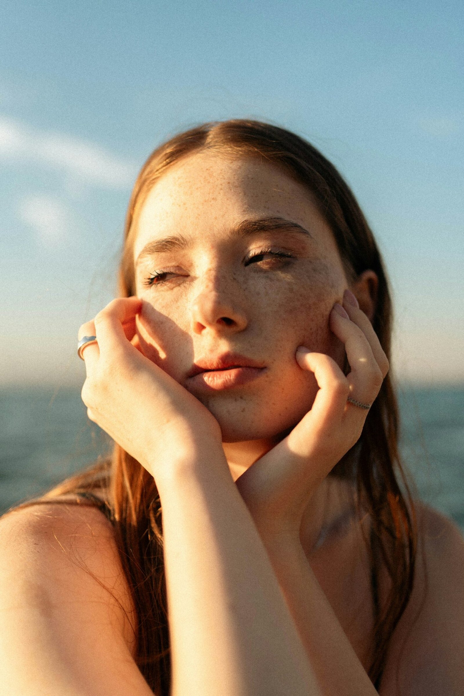 A woman with freckles resting her face in her hands in golden hour light