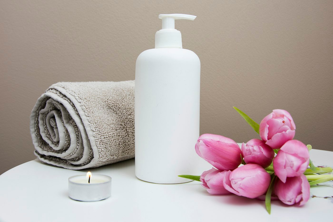 White plastic pump bottle beside pink tulips and gray towel